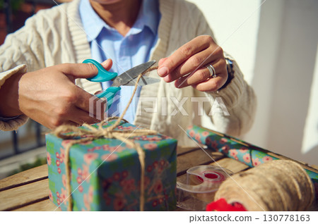 Close-Up of Hands Wrapping a Gift Box with Decorative Paper and Twine 130778163