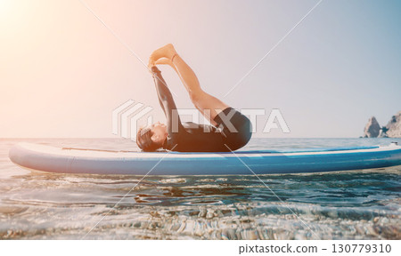 Yoga Paddle Board Man Beach - A man practices yoga on a paddle board in the ocean on a sunny day. 130779310