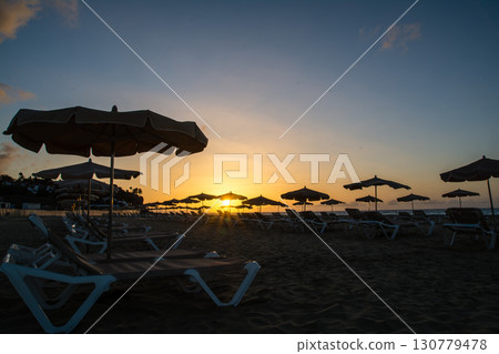 耀眼的朝陽從地平線升起，沙灘床和遮陽傘排列在富埃特文圖拉島的沙灘上 130779478