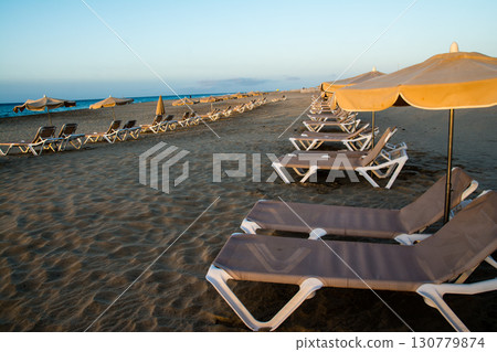 加那利群島富埃特文圖拉島上，沙灘床和遮陽傘排列在沐浴在清晨陽光下的沙灘海岸線上 130779874