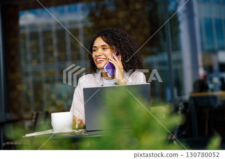 A woman is engaged in an important phone call while simultaneously working on her laptop A woman is engaged in an important phone call while simultaneously working on her laptop 130780052