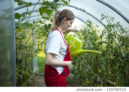 Pregnant woman watering plants in greenhouse with watering can 130780310