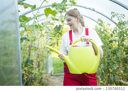 Woman watering plants in greenhouse with yellow watering can Woman watering plants in greenhouse with yellow watering can 130780312