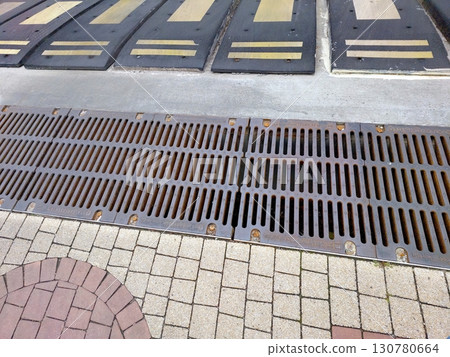 Sewer Grate Marking Entrance to Underground Parking Lot Surrounded by Patterned Pavement 130780664