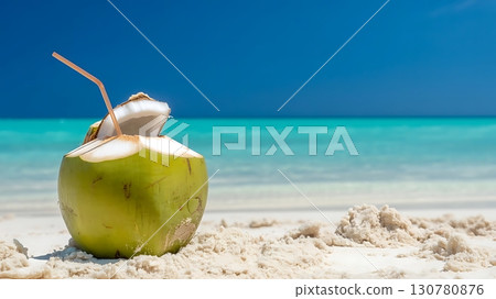 A coconut drink with a straw on a sandy beach with a blue ocean view 130780876