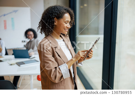 A professional woman is actively using a tablet while working in a modern office environment 130780955