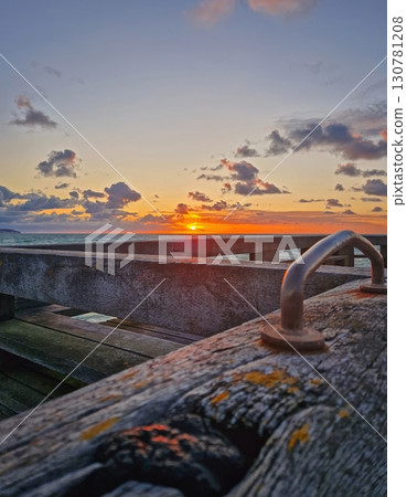 Stunning sunset over the sea, with the sun dipping below the horizon. Perspective from a wooden pier, showing its textured planks in the foreground. Peaceful evening atmosphere seaside Stunning sunset over the sea, with the sun dipping below the horizon. Perspective from a wooden pier, showing its textured planks in the foreground. Peaceful evening atmosphere seaside 130781208
