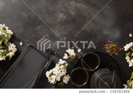 Black tea, cast iron kettle and blossom white flowers. Vertical composition with sakura bloom and petals. Japanese style and tea ceremony. Top view. Black tea, cast iron kettle and blossom white flowers. Vertical composition with sakura bloom and petals. Japanese style and tea ceremony. Top view. 130781408