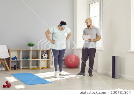 Male personal trainer checking progress of overweight woman in gym 130781564