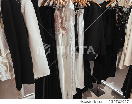 A curated collection of stylish clothing in a chic boutique. Display of clothing hanging on wooden hangers in a boutique, ideal for fashion retail. A curated collection of stylish clothing in a chic boutique. Display of clothing hanging on wooden hangers in a boutique, ideal for fashion retail. 130782027
