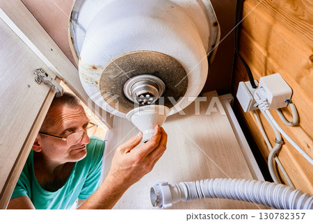 Sink drain assembly mounting, plumber installing plastic tailpiece under kitchen basin. 130782357