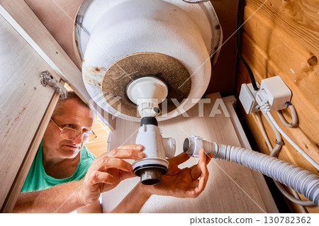 Plumber is dismantling leaking bottle trap with dishwasher hose spigot under kitchen sink to replace it with new one. 130782362