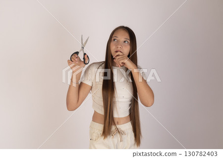 Little girl is holding a pair of scissors in one hand, bringing the other hand Little girl is holding a pair of scissors in one hand, bringing the other hand 130782403