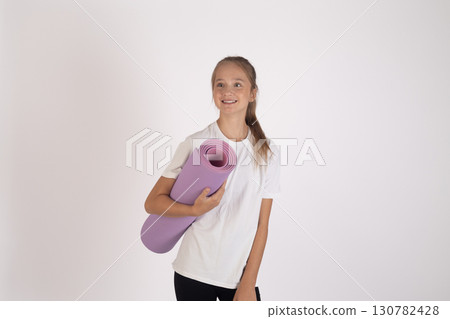 The girl is standing and smiling while holding a rolled-up yoga mat The girl is standing and smiling while holding a rolled-up yoga mat 130782428