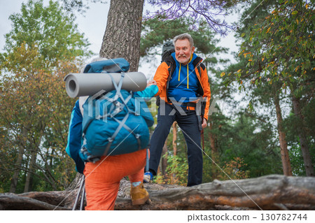 Hiking adventure. Man helping hand woman on hiking in forest. Senior couple enjoying outdoor recreation hiking. Happy old people backpackers hikers enjoy walking hike trekking tourism active vacation Hiking adventure. Man helping hand woman on hiking in forest. Senior couple enjoying outdoor recreation hiking. Happy old people backpackers hikers enjoy walking hike trekking tourism active vacation 130782744