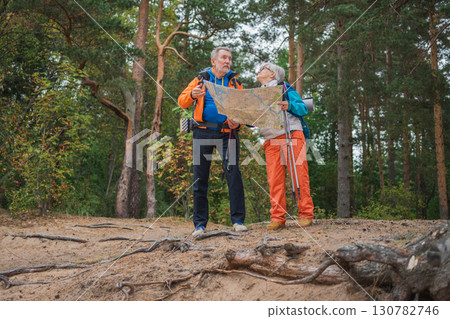 Hiking tourism. Senior couple man woman looking track in paper map enjoying hiking in forest. Happy old people backpackers hikers enjoy walking hike trekking tourism active vacation beauty of nature Hiking tourism. Senior couple man woman looking track in paper map enjoying hiking in forest. Happy old people backpackers hikers enjoy walking hike trekking tourism active vacation beauty of nature 130782746