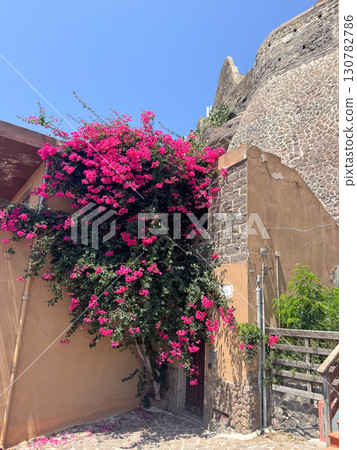 Stunning display of vibrant pink bougainvillea cascading over an old rustic stone wall. The vivid flowers contrast beautifully with the muted earthy tones, creating a picturesque scene. Stunning display of vibrant pink bougainvillea cascading over an old rustic stone wall. The vivid flowers contrast beautifully with the muted earthy tones, creating a picturesque scene. 130782786