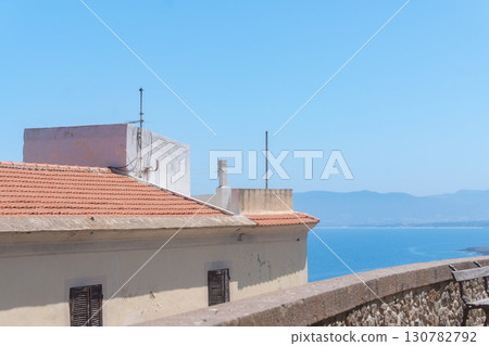 Rooftop with terracotta tiles overlooks a stunning coastal view. The ocean and mountains in the background create a serene and picturesque scene under a clear blue sky. Rooftop with terracotta tiles overlooks a stunning coastal view. The ocean and mountains in the background create a serene and picturesque scene under a clear blue sky. 130782792