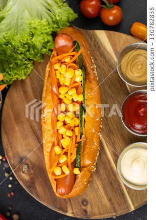 Classic hot dog with vegetables, sauces and sesame bun on black background. Street food Classic hot dog with vegetables, sauces and sesame bun on black background. Street food 130782838