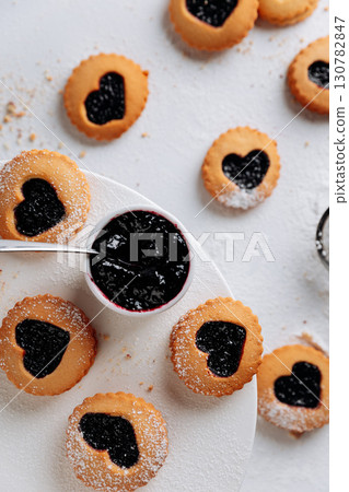Heart-shaped jam cookies with powdered sugar on white background, romantic baking scene Heart-shaped jam cookies with powdered sugar on white background, romantic baking scene 130782847