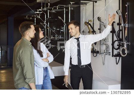 Salesman Assisting Couple With Shower Tap Selection At Plumbing Store Salesman Assisting Couple With Shower Tap Selection At Plumbing Store 130782895