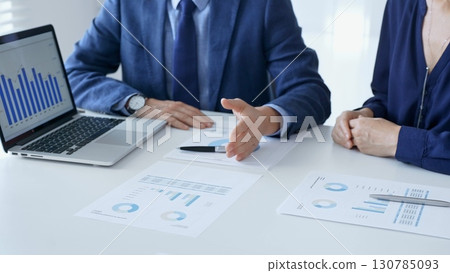 Business partners are discussing company performance and making plans based on charts and graphs displayed on laptop and printed documents. Businesspeople and finance 130785093