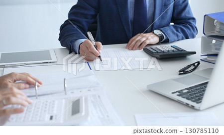 Close up of female accountant hands using calculator while collaborating with male colleague in office, calculating taxes and analyzing financial data. Audit and taxes in business 130785110