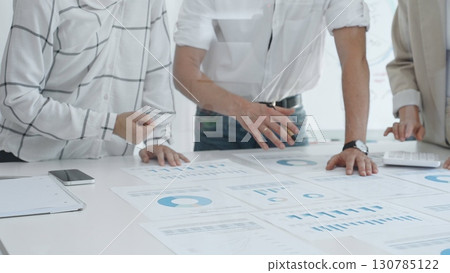 Professional team reviewing financial charts, working together in contemporary workspace, brainstorming strategic improvements. Business people concept 130785122