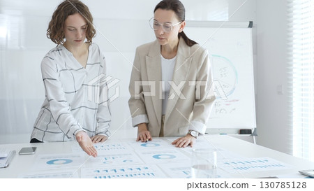 Two businesswomen are examining financial charts and statistics during a productive meeting in a modern office, demonstrating teamwork and strategic planning. Business people concept Two businesswomen are examining financial charts and statistics during a productive meeting in a modern office, demonstrating teamwork and strategic planning. Business people concept 130785128