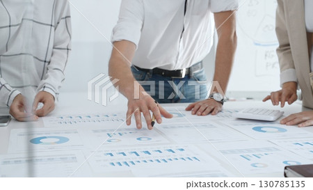Professional team reviewing financial charts, working together in contemporary workspace, brainstorming strategic improvements. Business people concept 130785135