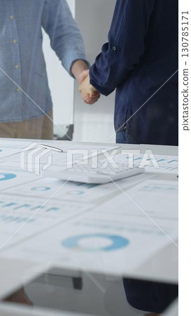 Business partners shaking hands after successful agreement over financial documents, calculator and pen on white table in office. Handshake concept Business partners shaking hands after successful agreement over financial documents, calculator and pen on white table in office. Handshake concept 130785171