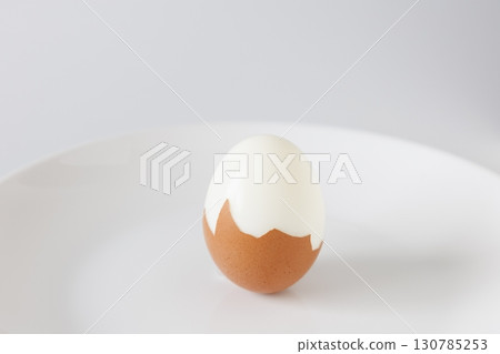 Half-peeled boiled egg on a white plate 130785253