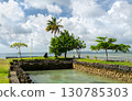 A scenic view of the coastline on Koror island, Palau, featuring a stone inlet, green trees, and the Pacific Ocean under a cloudy sky 130785303