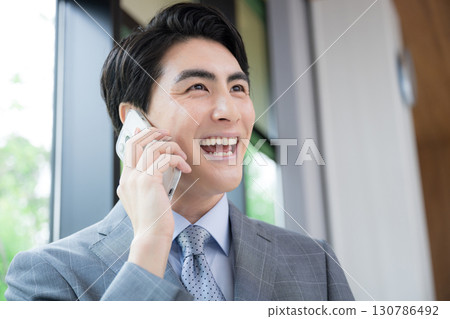 Profile image of a businessman in a suit making a phone call by a window with fresh greenery 130786492