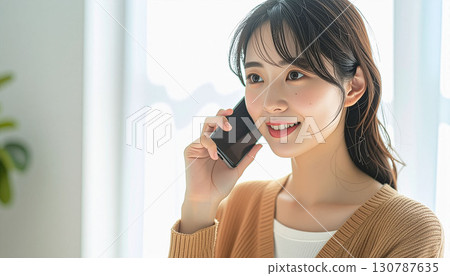 A young woman talking on a smartphone in a bright room 130787635