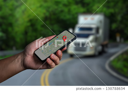 Hand holding smartphone with GPS navigation map and location pin, truck driving on curved road in background, concept of transportation, delivery tracking, logistics, and navigation technology. Hand holding smartphone with GPS navigation map and location pin, truck driving on curved road in background, concept of transportation, delivery tracking, logistics, and navigation technology. 130788634
