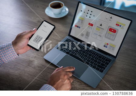 Mobile app interface concept with designer using smartphone and laptop, showing wireframe and UI UX layout on screen, symbolizing application development, digital design, and user experience. 130788636