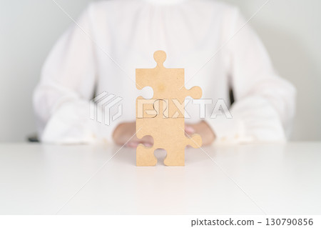 Woman connecting couple puzzle piece, wood jigsaw on table. Business solutions, mission, success, goals, strategy, Teamwork, Idea, Solution and challenge concepts 130790856