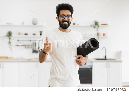 Man of South Asian origin, young adult with beard, wearing casual clothing, smiling. Modern kitchen interior background suggests active home lifestyle and fitness focus. 130792080