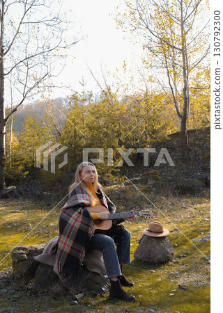 Portrait of smiling caucasian artist plays wooden acoustic guitar in autumnal park. Young songwriter plays string musical instrument hobby outside in nature fall time. Audio music healing Portrait of smiling caucasian artist plays wooden acoustic guitar in autumnal park. Young songwriter plays string musical instrument hobby outside in nature fall time. Audio music healing 130792300