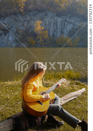 Blonde woman playing string guitar outdoors in autumn forest. Concept of sound therapy, mental health and wellness rituals. Calmness tranquility audio-sensory practices. Aura farming energy Blonde woman playing string guitar outdoors in autumn forest. Concept of sound therapy, mental health and wellness rituals. Calmness tranquility audio-sensory practices. Aura farming energy 130792314