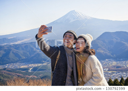 Tourist scene of a young couple smiling and taking a selfie with Mount Fuji in the background 130792399