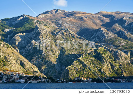 A panoramic view of the majestic mountains of Montenegro towering over a small coastal town. The photo highlights the scale and natural beauty of the landscape. A panoramic view of the majestic mountains of Montenegro towering over a small coastal town. The photo highlights the scale and natural beauty of the landscape. 130793020