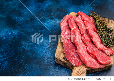 Beautifully sliced raw buffalo meat on a rustic platter, showcasing its appealing color and quality, perfect for grilling or roasting. blue background. top view 130794005