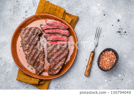 Tender flat iron steak, grilled to enhance its natural flavors and tenderness. grey background. top view Tender flat iron steak, grilled to enhance its natural flavors and tenderness. grey background. top view 130794049