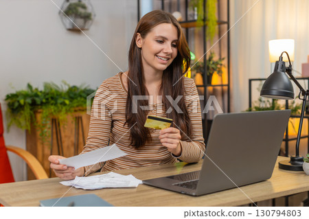Young woman enters credit card number on laptop pays bills checks totals and presses pay to confirm 130794803