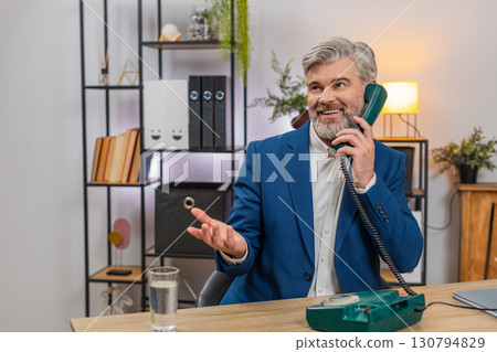Middle-aged businessman smiles nostalgically speaking on retro cord phone from 90s during work break 130794829