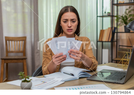 Young woman shocked by huge utility bill raises eyebrows then throws papers onto desk in disbelief 130794864