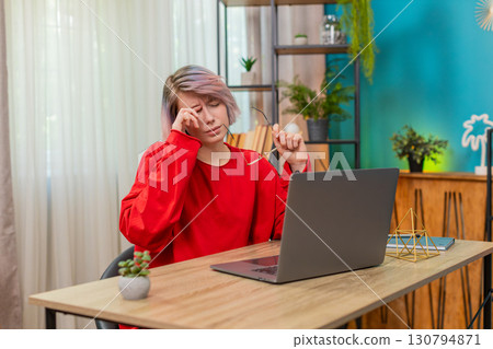 Young woman rubbing eyes removing glasses feeling tired eye strain during remote laptop work at home 130794871
