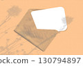 Natural light casts shadows from wildflowers on an envelope with a sheet of white paper lying on an orange background. Mockup 130794897